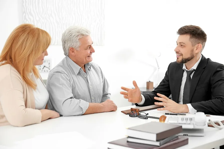 An older couple has a discussion with a man in a suit at an office table.